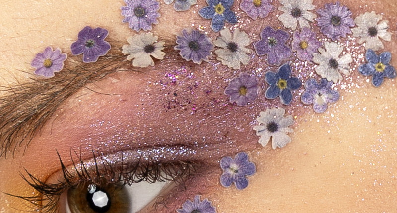 Bloemetjes in wax paars, wit en blauw rond het oog gedragen bij een flower power-look
