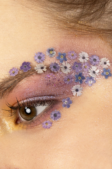 Bloemetjes in wax paars, wit en blauw rond het oog gedragen bij een flower power-look