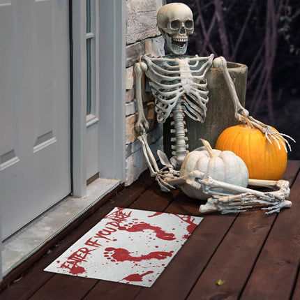 Deurmat met bloedsporen voor de voordeur naast een skelet en pompoenen op een halloweenentree
