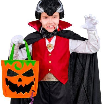 Jongen draagt oranje pompoentas aan groene hengsels tijdens trick or treat