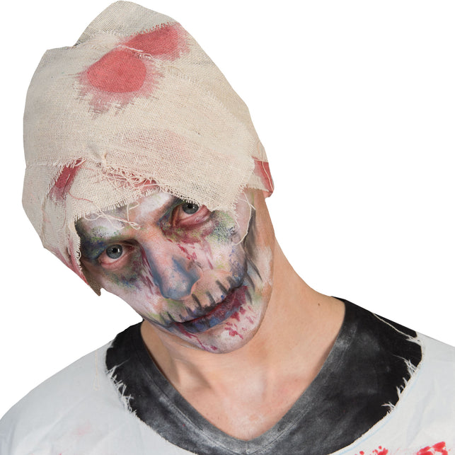 Nepwondenverband om het hoofd gedraaid bij een bleek geschminkt zombiegezicht voor Halloween