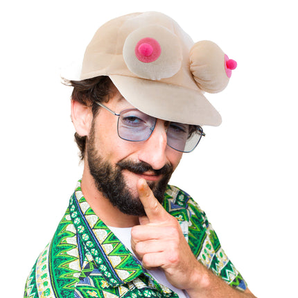 Pet met borsten met roze tepels en brede klep, gedragen door een man met bril voor een vrijgezellenavond