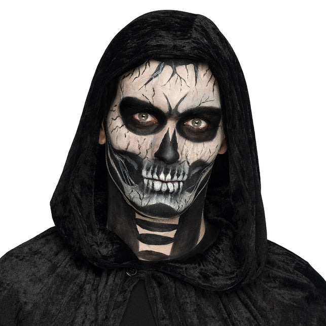 Skeletgezicht geschminkt met de doodskop schminkset, zwarte oogkassen en witte tanden voor Halloween