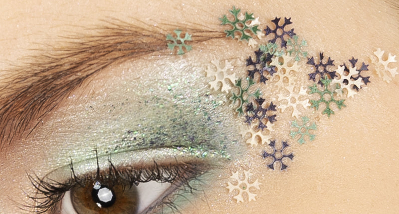 Sneeuwvlokjes schmink in wax op ooglid, witte, groene en paarse vlokjes over groene oogmake-up