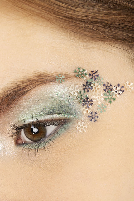 Sneeuwvlokjes schmink in wax op ooglid, witte, groene en paarse vlokjes over groene oogmake-up